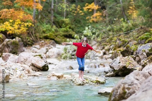 Fototapeta Naklejka Na Ścianę i Meble -  Boy trying to cross a wild mountain river jumping on stones