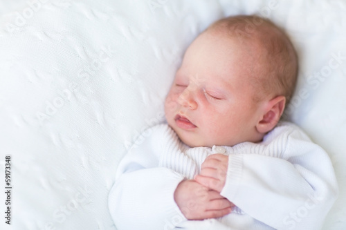 Sweet newborn baby sleeping on a white knitted blanket