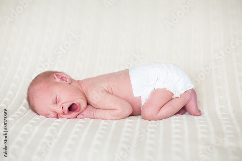 Yawning newborn baby in a diaper sleeping on a knitted blanket