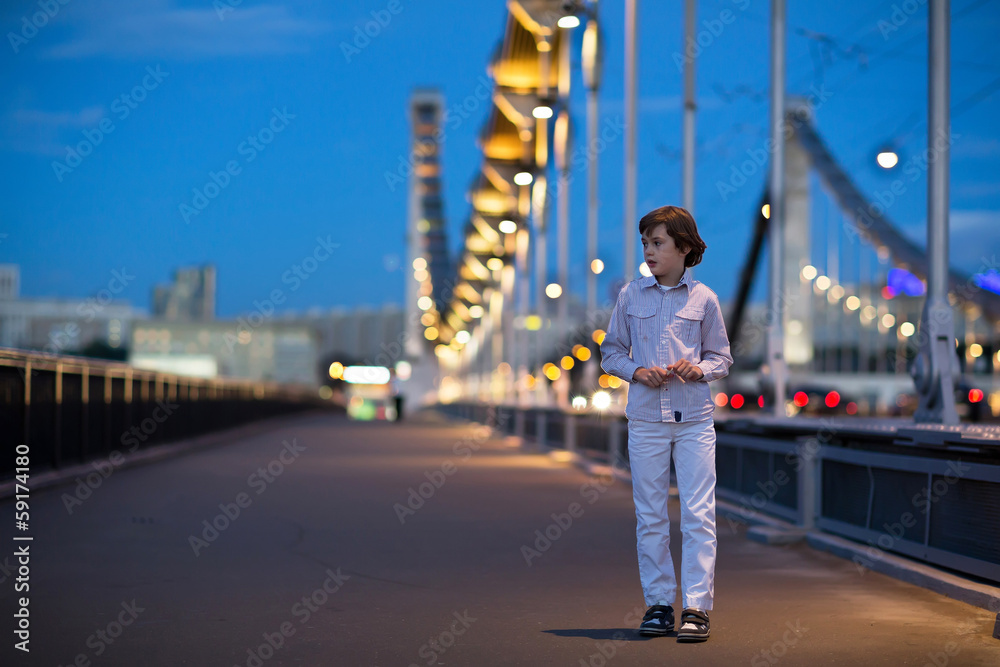 Fototapeta premium Little boy walking alone scared on a beautiful bridge in a dark