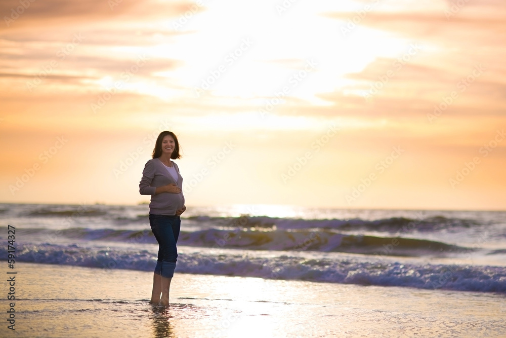 Silhouette of a young pregnant woman with a sunset at a beach