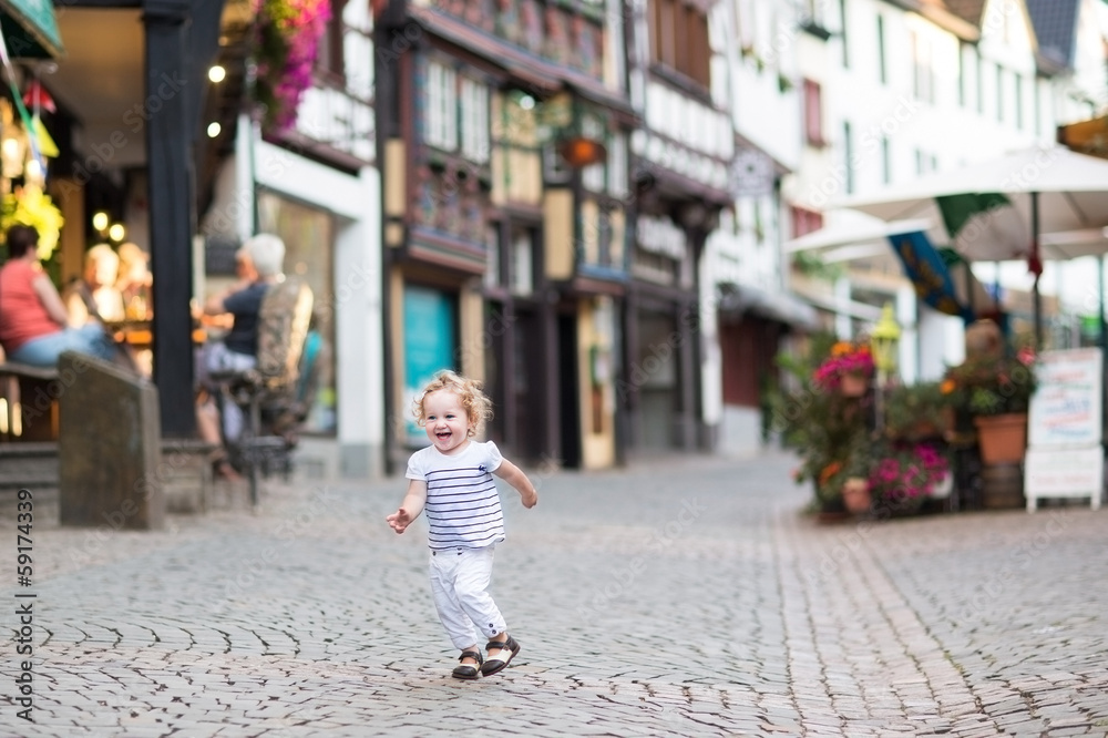 Little baby girl running in a street of a historical city