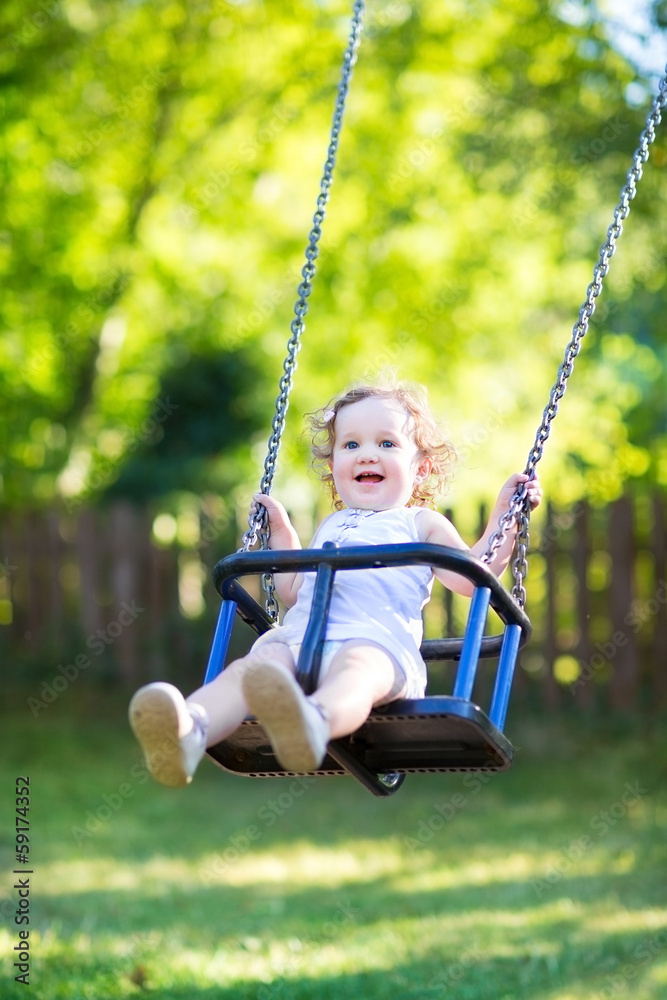 Adorable baby girl with big eyes and curly hair on a swing Adorable baby girl with big eyes and curly hair on a swing