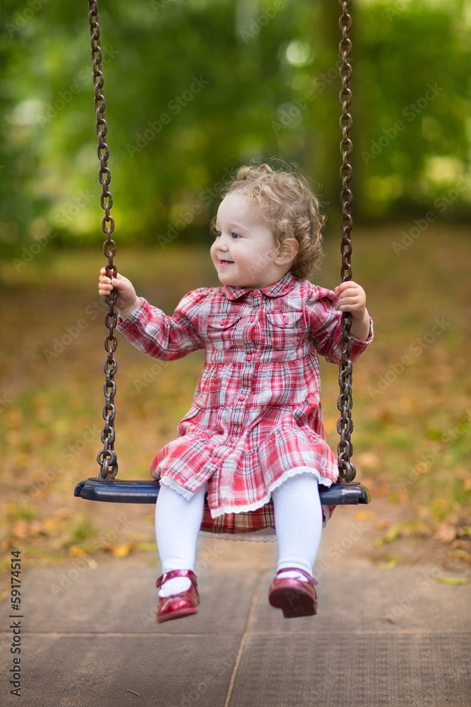 Baby girl with beautiful curly hair wearing a red dress in swing