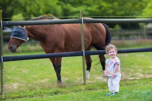 Cute funny baby playing with a horse on a farm in summer