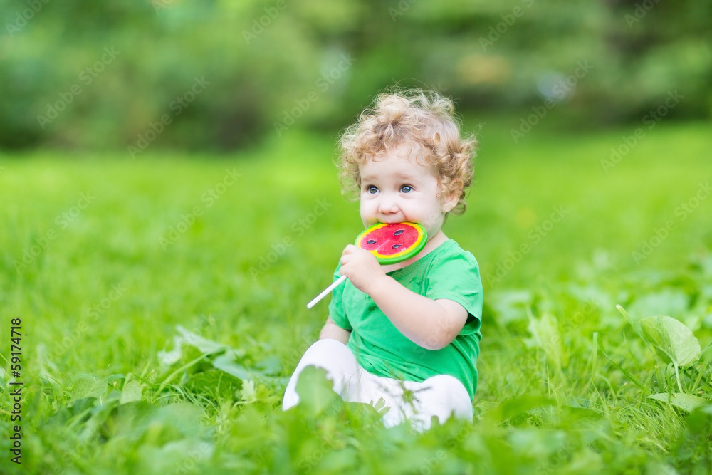 Сurly baby girl eating watermelon candy in a summer park Сurly baby girl eating watermelon candy in a summer park