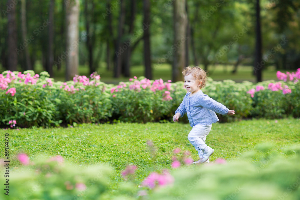 Curly baby girl running in a beautiful park among pink flowers