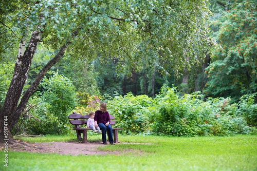 Grandmother and baby girl in a park on a bench under a tree
