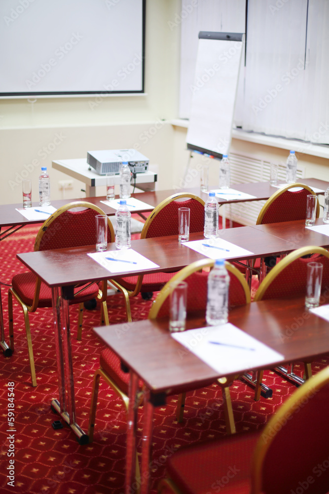 Tables with bottles, sheets, pens, rows of chairs and projector Tables with bottles, sheets, pens, rows of chairs and projector