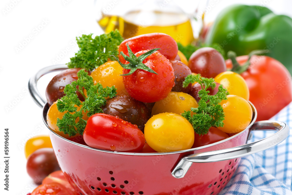 Assorted cherry tomatoes and greens in a colander, close-up