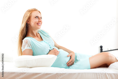 Cheerful pregnant blond sitting on white sheet in bed