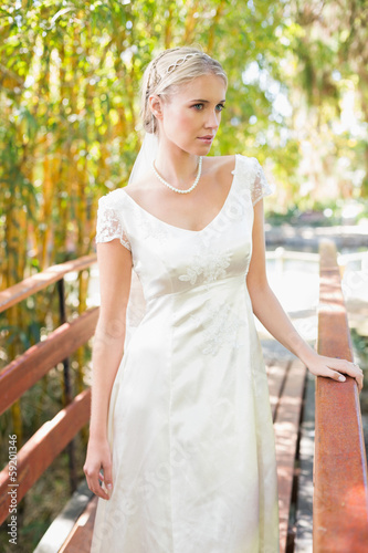 Content blonde bride in pearl necklace standing on a bridge