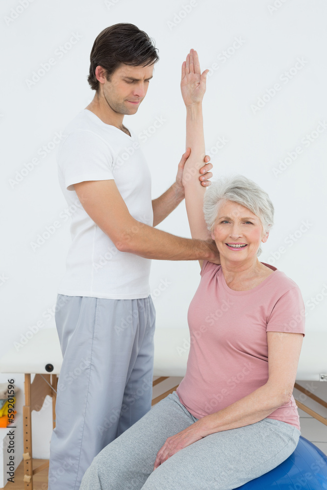 Obraz premium Senior woman on yoga ball with a physical therapist