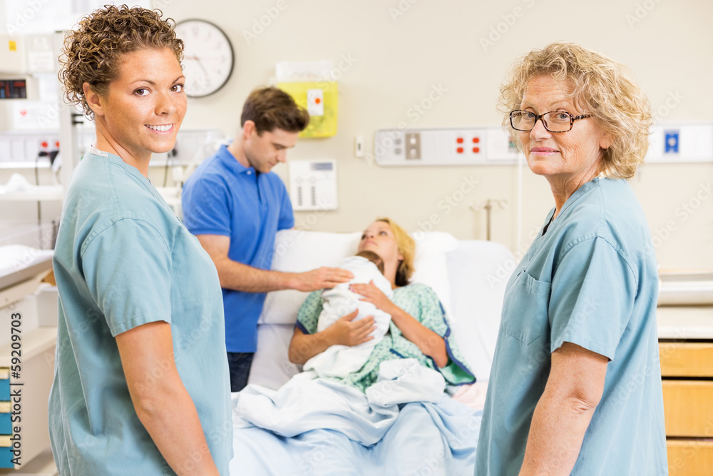 Obraz premium Successful Nurses Standing Against Couple With Baby In Backgroun