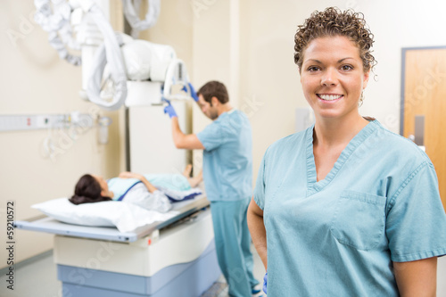 Nurse Smiling While Colleague Preparing Patient For Xray