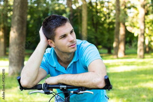 Thoughtful young man leaning on a bicycle