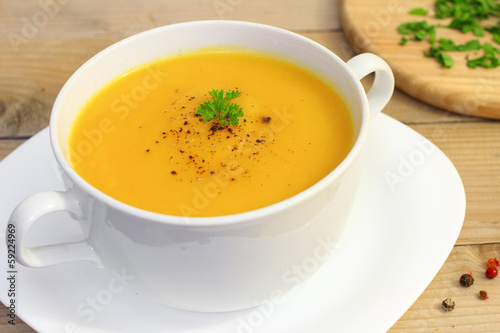 Vegetarian pumpkin soup in white bowl on wooden table