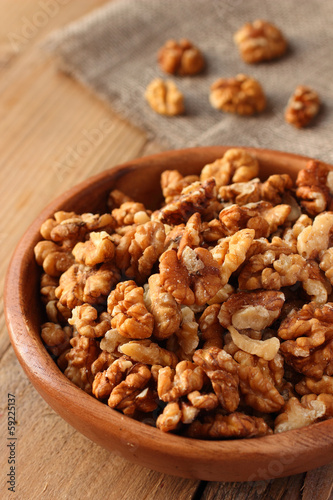 Shelled walnuts in wooden bowl on wooden background