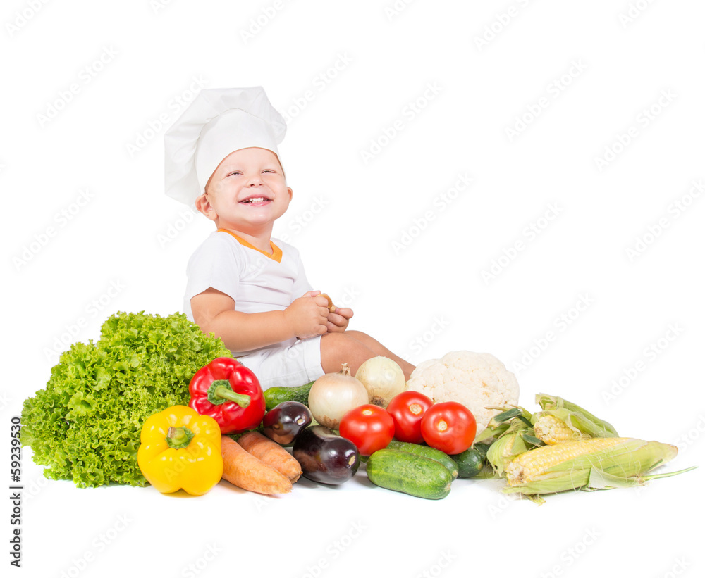 happy small kitchen boy in cook cap around variegated vegetables happy small kitchen boy in cook cap around variegated vegetables