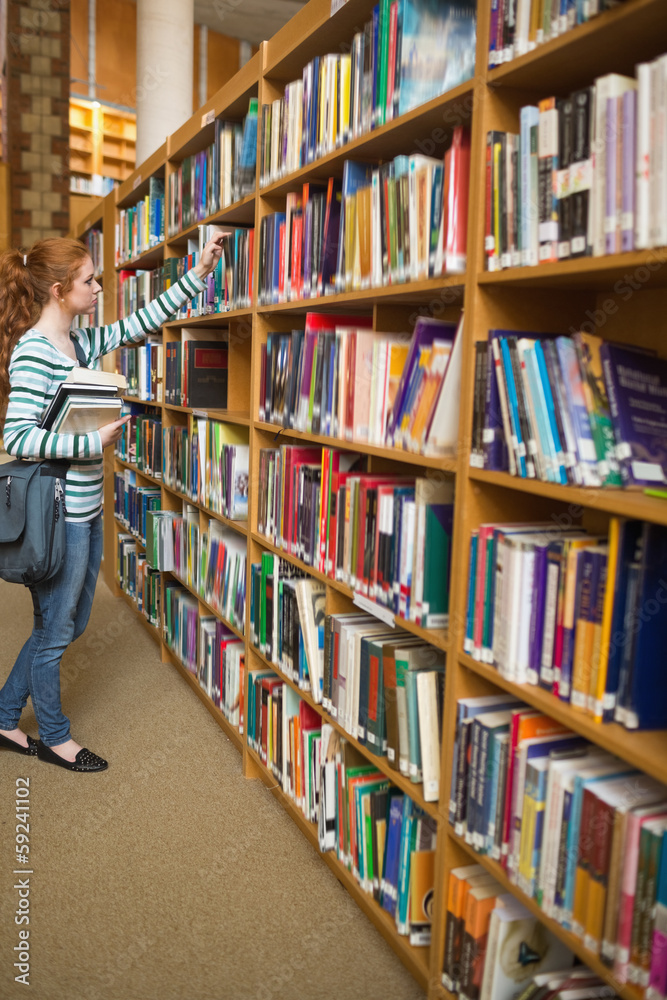 Redhead student taking book from bookshelf in the library Redhead student taking book from bookshelf in the library
