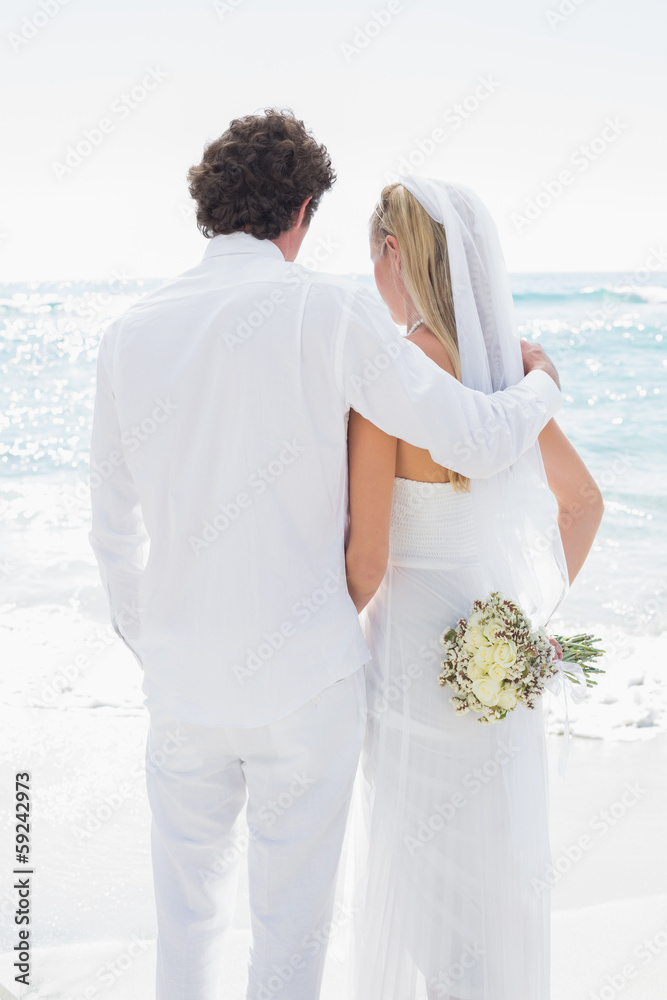 Fototapeta premium Bride and groom looking out to sea embracing