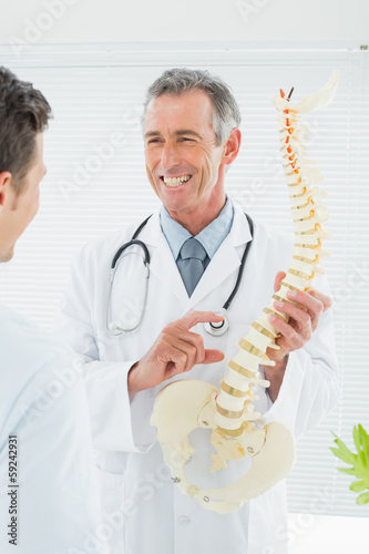 Cheerful doctor explaining spine to patient in office