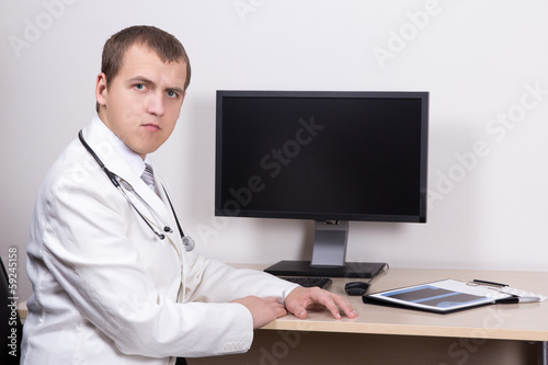 young male doctor sitting with computer in office