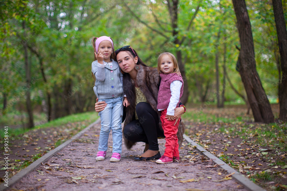 Young mother with her little daughters looking to camera oudoor Young mother with her little daughters looking to camera oudoor