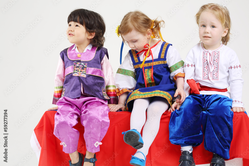 Two little boys and girl in folk costumes sit and look Two little boys and girl in folk costumes sit and look