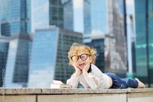 Little cute girl in glasses with book lies on border and laughs