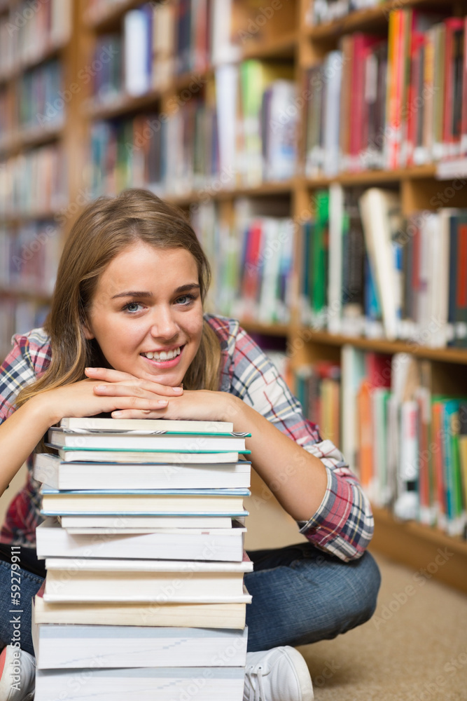 Happy student sitting on library floor leaning on pile of books Happy student sitting on library floor leaning on pile of books