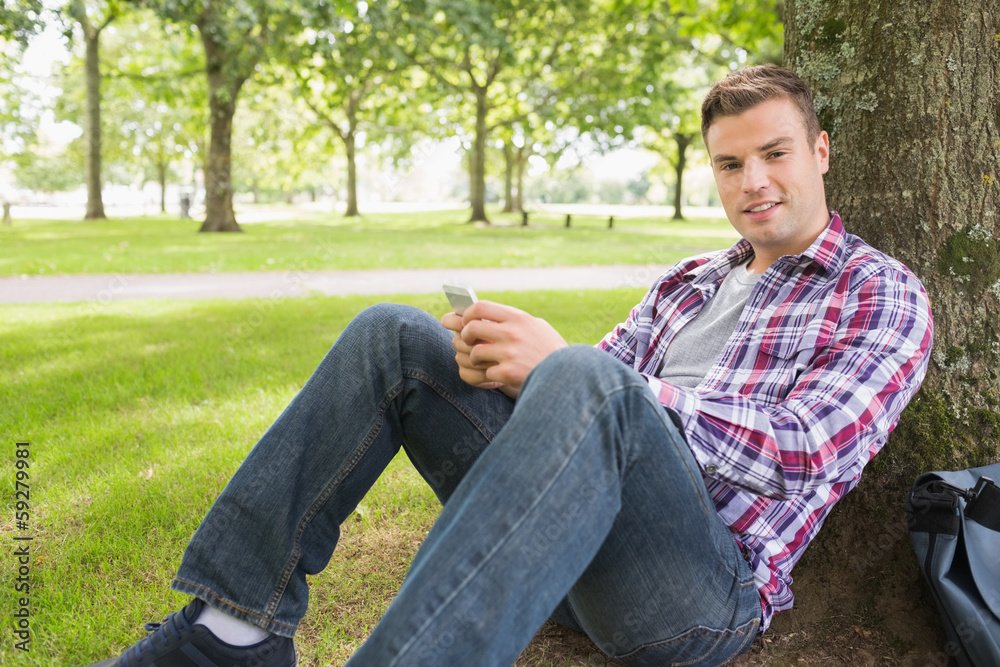 Cheerful student sending a text outside leaning on tree Cheerful student sending a text outside leaning on tree