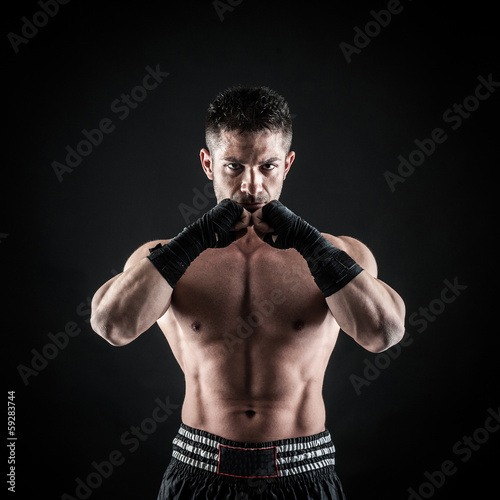 Sportsman kick boxer intense portrait against black background. © pio3