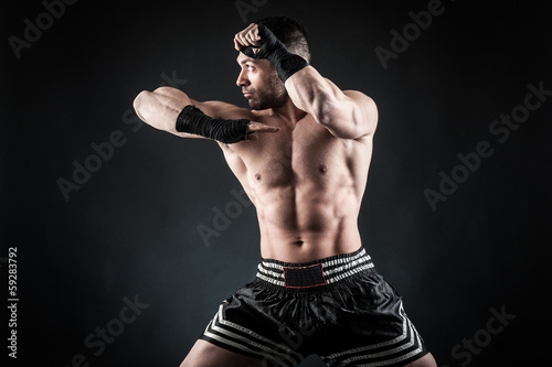 Sportsman kick boxer fighting against black background. © pio3