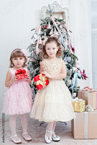 Two little girls with gifts near a Christmas fir-tree