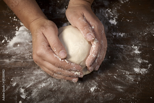 woman's hands kneading dough on wooden table