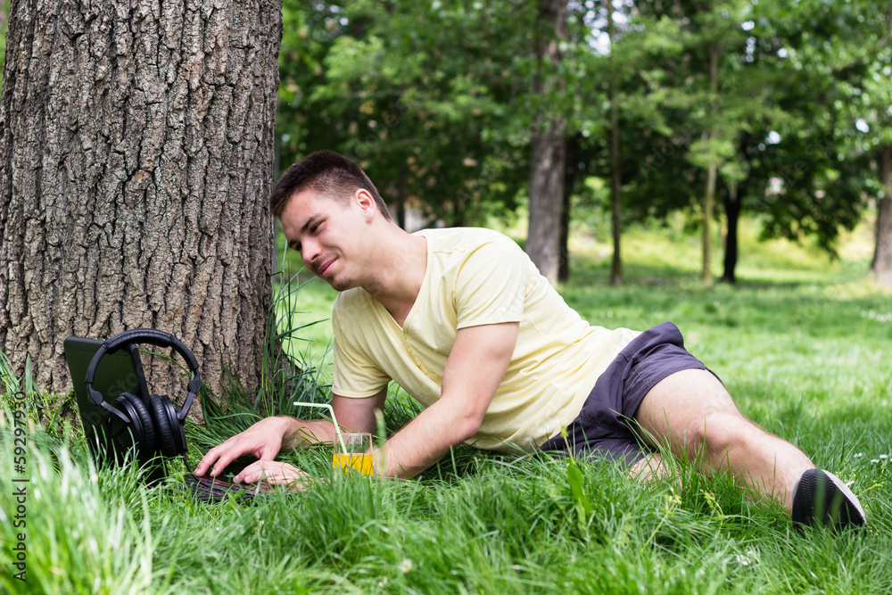 Cheerful young male using laptop in the park Cheerful young male using laptop in the park