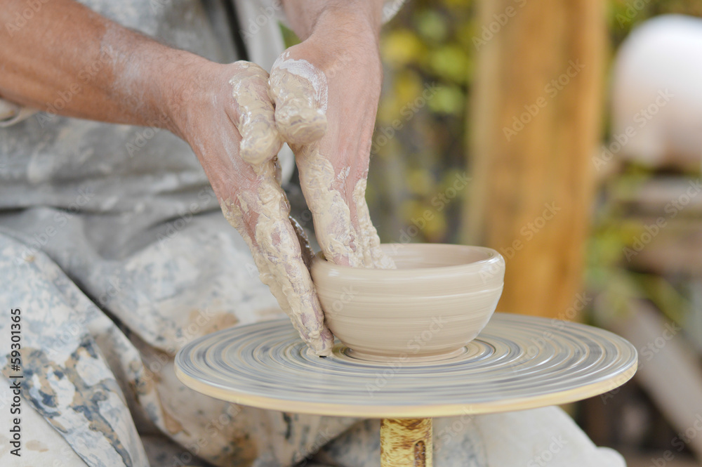 Craftsman making vase from fresh wet clay on pottery wheel