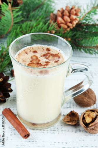 Cup of eggnog with fir branches on wooden background
