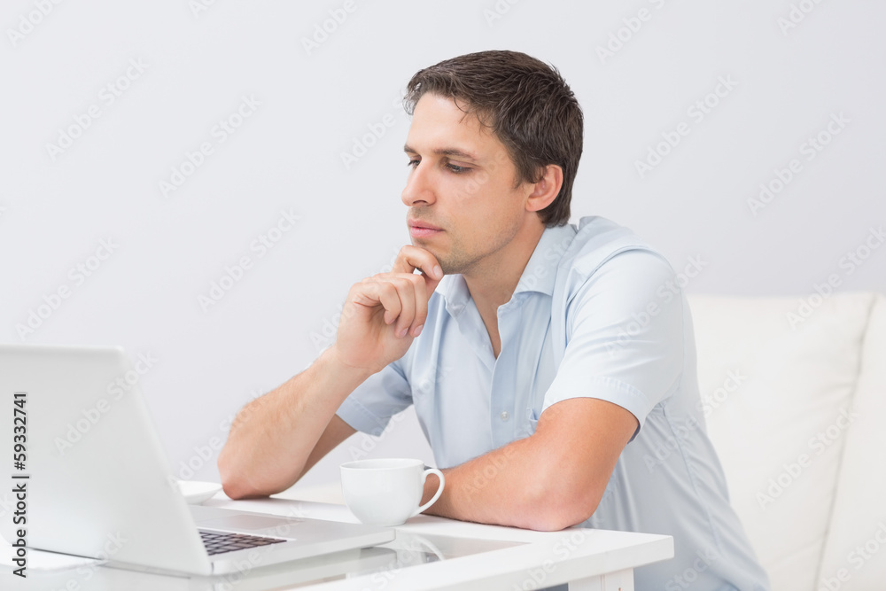 Side view of a serious man using laptop at home