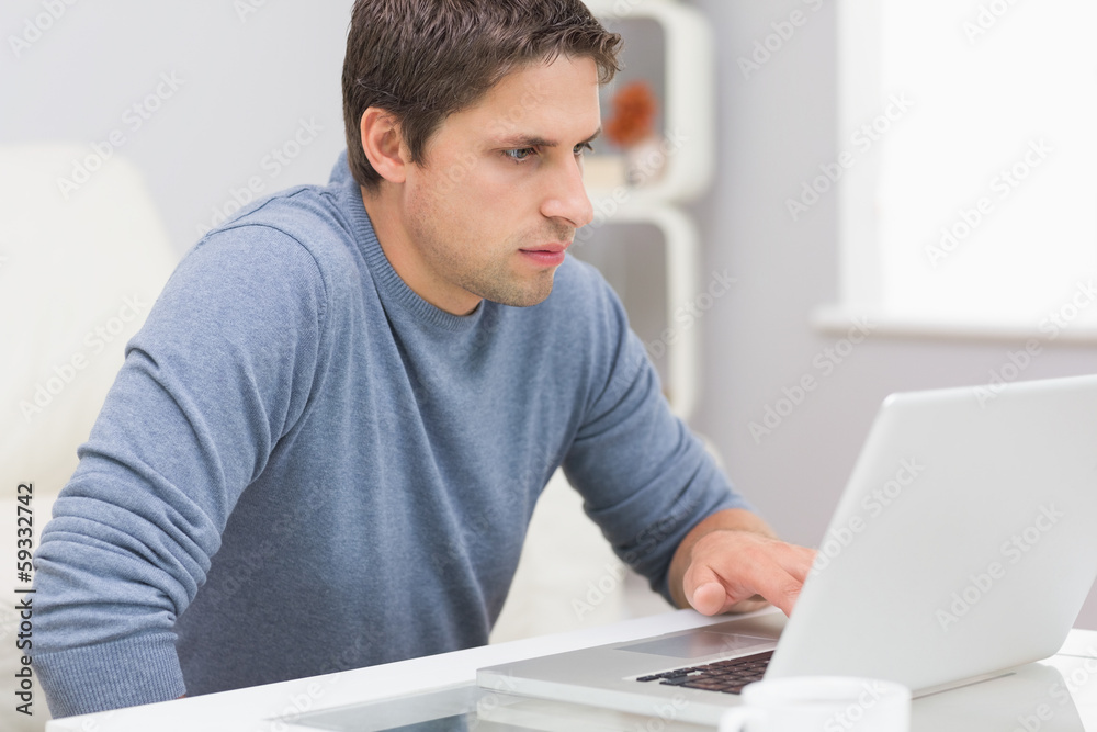 Serious young man using laptop in living room Serious young man using laptop in living room