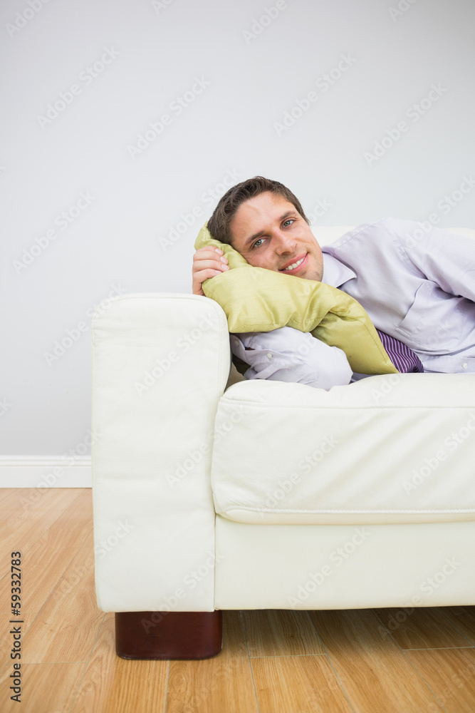 Smiling young businessman lying on sofa in living room