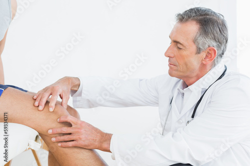 Side view of a mature doctor examining patients knee