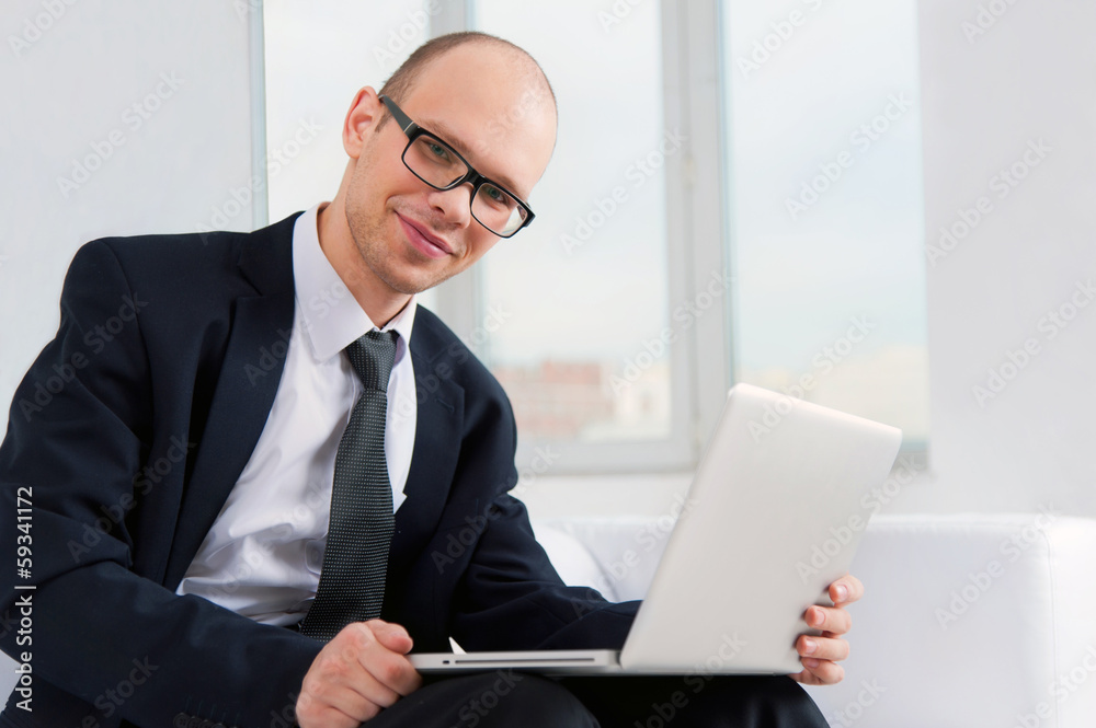 Young smiling businessman sitting on couch with laptop Young smiling businessman sitting on couch with laptop