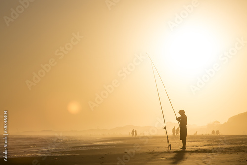 Pescador pescando en la playa al atardecer.