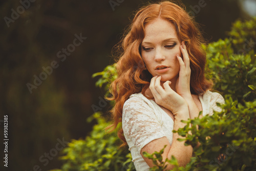 Portrait of young beautiful redhair woman standing in green park photo