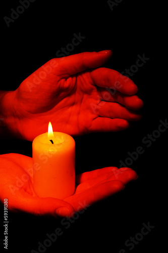 Burning candle in hands isolated on black