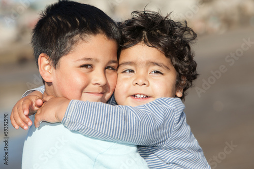 Fotografía close up portrait of two cute little hispanic brothers hugging each other on a s