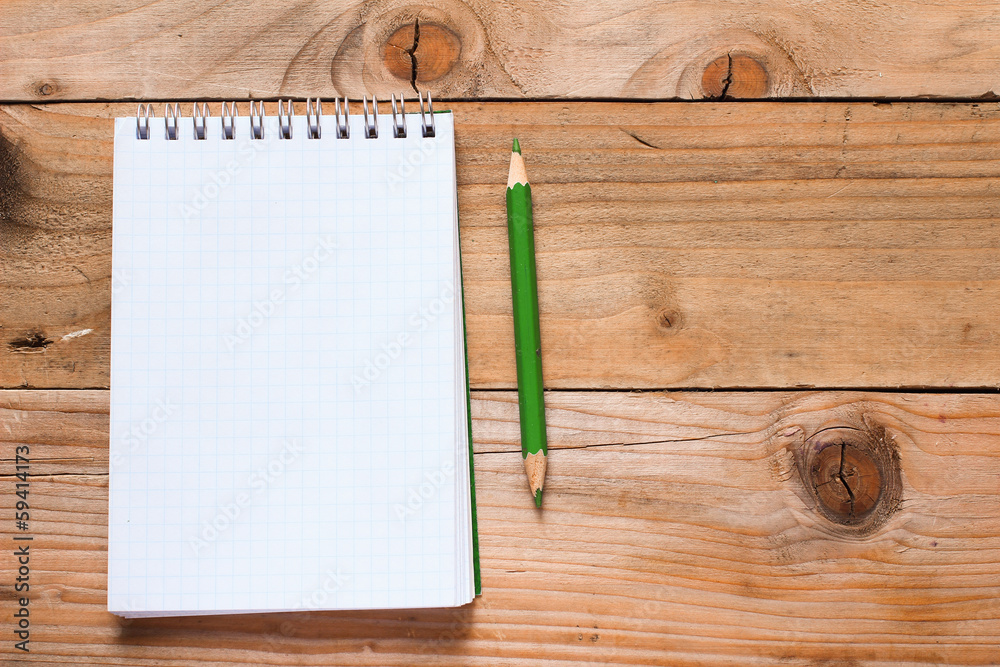 Notebook with green pencil on wooden table Notebook with green pencil on wooden table
