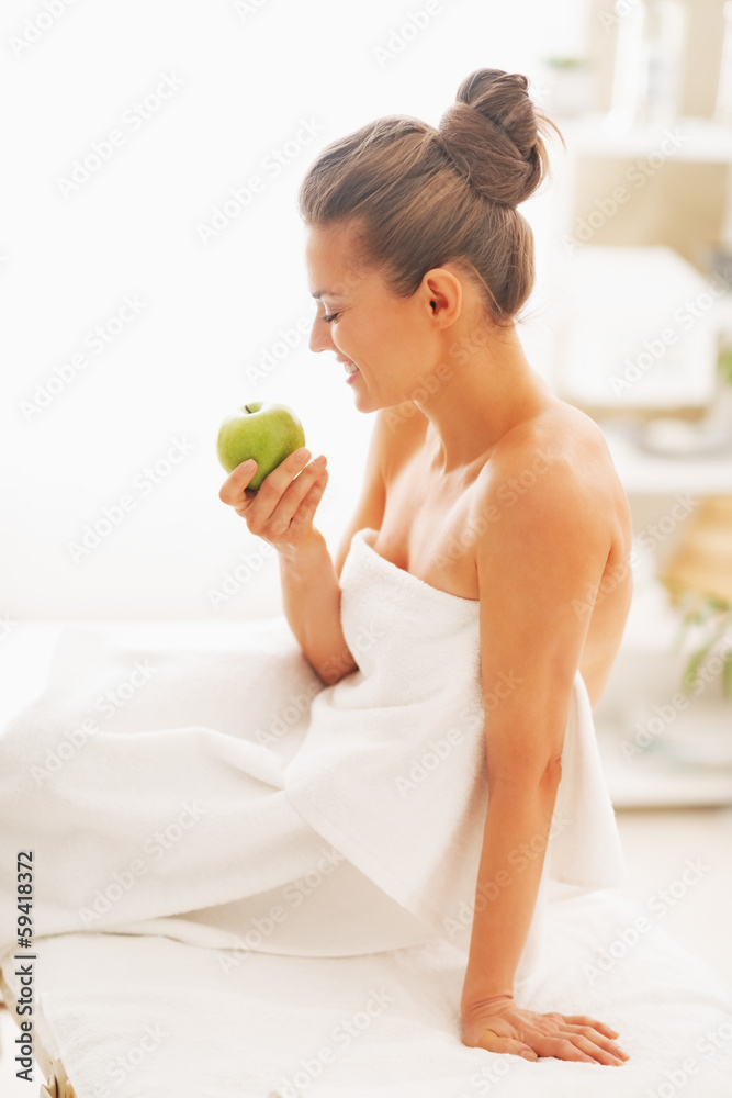 Happy young woman with apple sitting on massage table Happy young woman with apple sitting on massage table